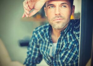 Man in plaid shirt gazing thoughtfully outside.